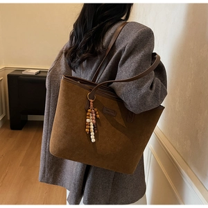 Détail du sac cabas en daim marron foncé avec anses en cuir et breloque en bois rétro