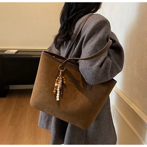 Detail of a brown suede tote bag featuring a vintage wooden beaded tassel charm