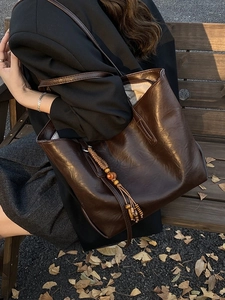 Brown vintage faux leather tote bag with boho tassel displayed on an autumn park bench