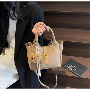 Détails du sac seau beige à motif litchi avec fermoir doré et breloque ours en peluche