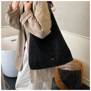 Detail of a large black vintage tote bag in matte leather worn by a model in a cozy room