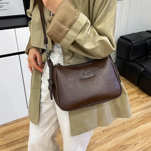 Detail of dark brown leather crossbody bag featuring silver kangaroo logo and zip closure