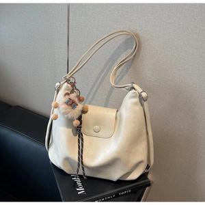 Dettaglio della borsa hobo in ecopelle bianco crema con ciondolo a leone e tracolla regolabile
