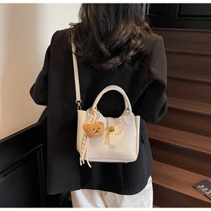 Détail du sac seau blanc à motif litchi avec fermoir doré et pendentif en peluche