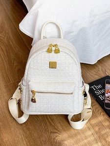 Elegant white tweed backpack with gold hardware displayed on a cozy wooden floor