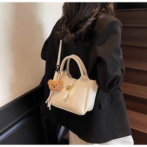 Détail d'un sac seau en cuir blanc avec fermoir doré et breloque petit ours