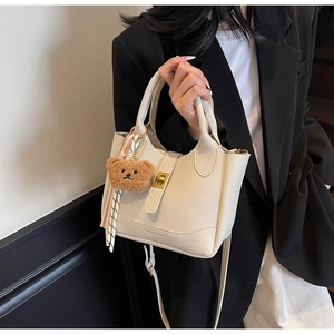 Détail du sac seau en cuir litchi crème avec boucle dorée et breloque petit ours
