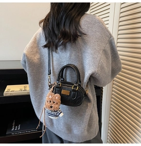 Detail showing a black mini boston bag with a cute brown plush dog charm and gold plaque