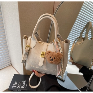 Détail d'un sac seau blanc en cuir grainé avec fermoir doré et pendentif ours en peluche