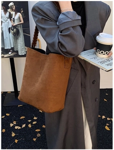 Detail of caramel suede bucket bag with woven shoulder strap in an autumn setting