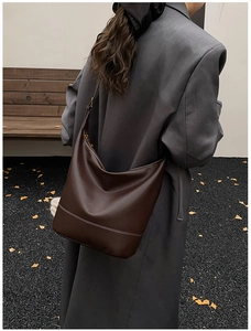 Detail of soft brown leather hobo bag with contrast white stitching and foliage background