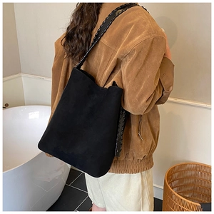 Detail of a large black suede bucket bag with wide woven shoulder strap on a model
