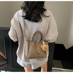 Vue détaillée d'un sac seau en cuir taupe avec un accessoire de breloque en forme d'ours