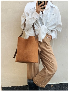 Close-up of brown suede bucket bag featuring a stylish woven shoulder strap detail