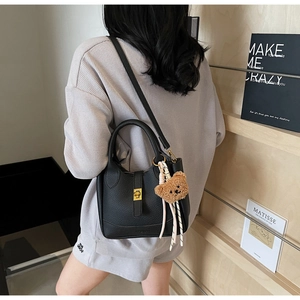 Détail d'un sac seau noir en cuir à motif litchi avec fermoir doré et petit ours