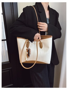 Detail of woven fabric tote with leather trim, wooden bead tassel and gold lettering