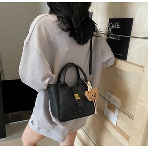 Détail du sac seau en cuir litchi noir avec fermoir doré et accessoire pendentif ours