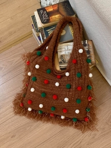 Brown knitted tote bag with colorful pom-poms and bohemian fringe detail on a books background