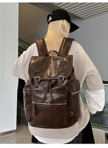Close-up of the dark brown leather backpack with metal buckles and multiple zip pockets