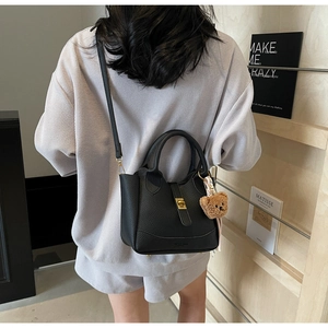 Détail d'un sac seau en cuir noir avec breloque ours porté à l'épaule par un mannequin