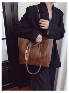 Detail of a brown woven tote bag with a decorative bead pendant and shoulder strap