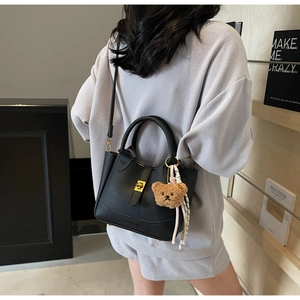 Sac seau en cuir à motif litchi avec fermoir doré et charme d'ours porté par un mannequin