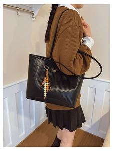 Detail of black woven texture tote bag featuring golden lettering and beaded tassel charm