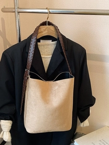 Large capacity camel suede bucket bag with brown woven strap on a wooden hanger