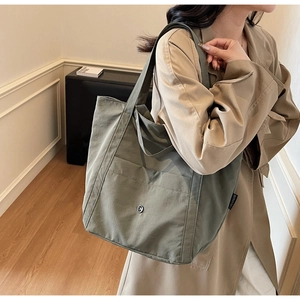 Detail of dark green canvas tote bag with side brand label and metal button pocket
