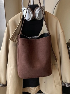 Brown suede bucket bag with woven leather strap on a trench coat, minimalist aesthetic