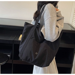 Detail of a large black tote bag featuring a side pocket and a round CM metal logo