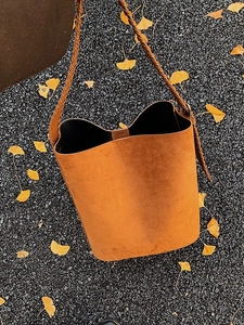 Caramel suede bucket bag with woven strap on autumn ginkgo leaves background