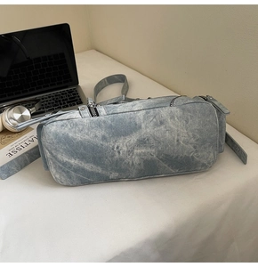 Gros plan sur un sac rectangulaire en denim délavé posé sur un bureau blanc avec accessoires