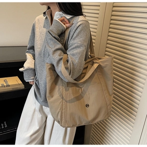 Detail of khaki nylon tote bag featuring front pocket with logo and double straps