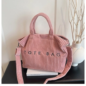 Pink corduroy tote bag detail showing black embroidered text and metal strap buckles