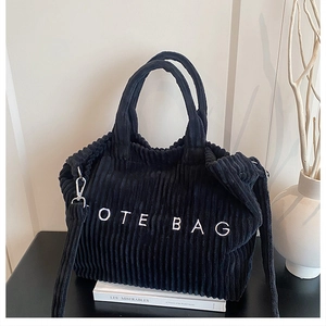 Detail of black corduroy tote bag featuring white embroidery and metallic strap rings