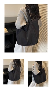 Detail of a black nylon tote bag showing front pocket and metallic logo buckle