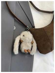 Detail of plush white rabbit charm on brown suede crescent bag with silver ring clasp