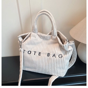 Close-up of white corduroy tote bag with black letter embroidery and adjustable strap