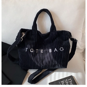 Detailed close-up of a black corduroy tote bag featuring white embroidered lettering