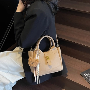 Sac seau beige à motif litchi avec pendentif ours sur des escaliers en bois