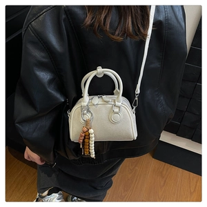 Close-up of white mini Boston bag with ethnic beaded charm on black leather jacket