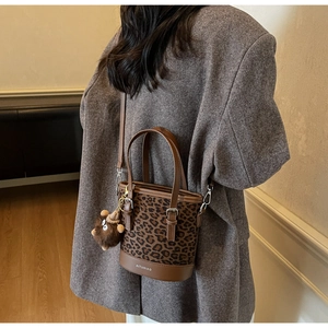 Détail du sac seau à motif léopard avec base en cuir et breloque peluche sur la bandoulière
