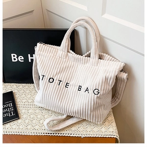 Close-up of white corduroy tote bag featuring black lettering and dual strap details