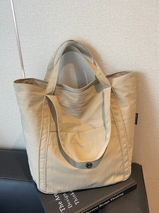 Minimalist khaki nylon tote bag with wide handles and logo detail on elegant dark base