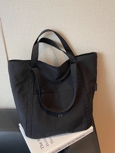 Minimalist black nylon tote bag with dual handles and metal logo on a book