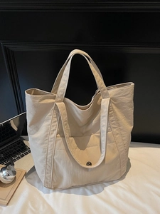 Large beige tote bag with front pocket on white bed, showing stylish minimalist design