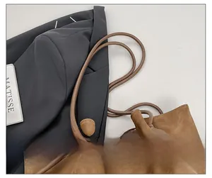 Close-up of brown suede bucket bag featuring cylindrical leather straps and drawstring detail