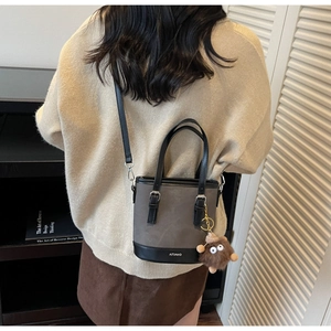 Détail d'un sac seau gris avec breloque en peluche et logo porté par un mannequin