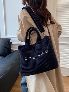 Black corduroy tote bag with TOTE BAG embroidery and adjustable strap on a model